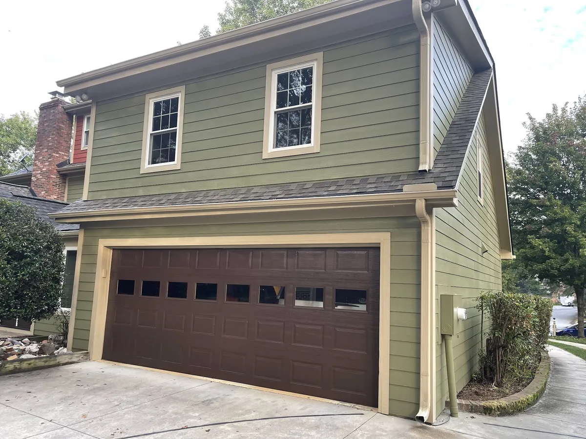 Two-story home with green siding, cream trim and a painted garage door