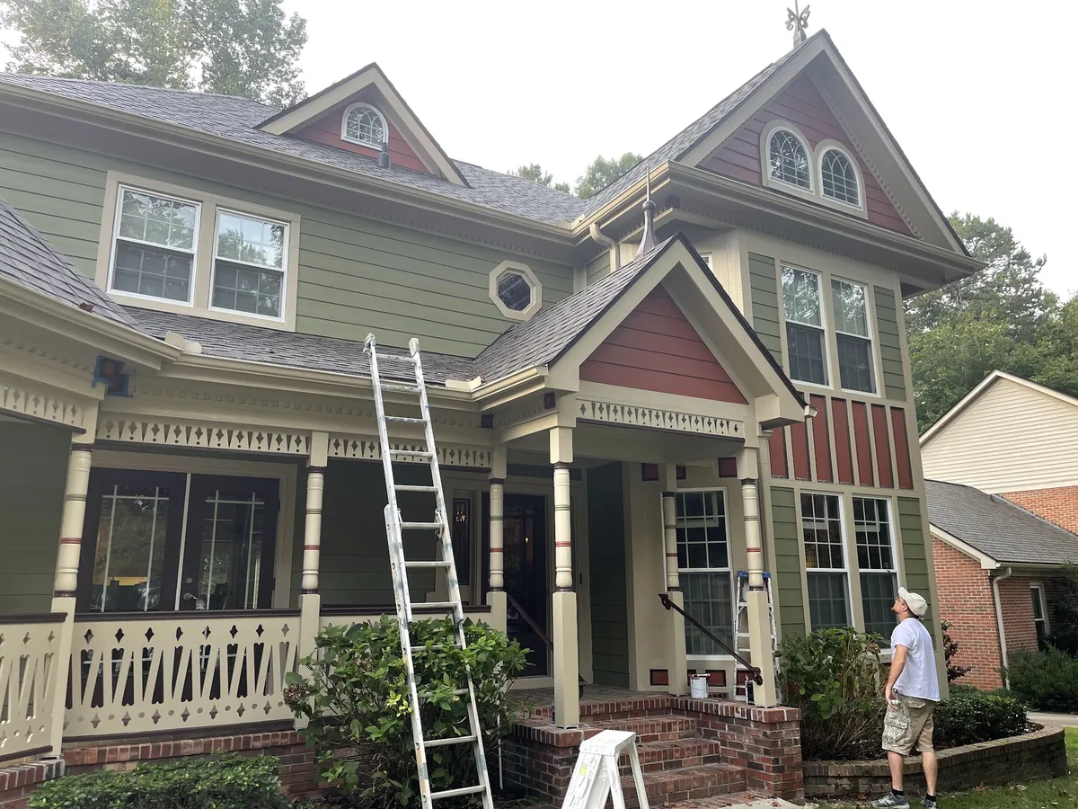 Craftsman home with multi-color siding, red gable accents and a painter on a ladder