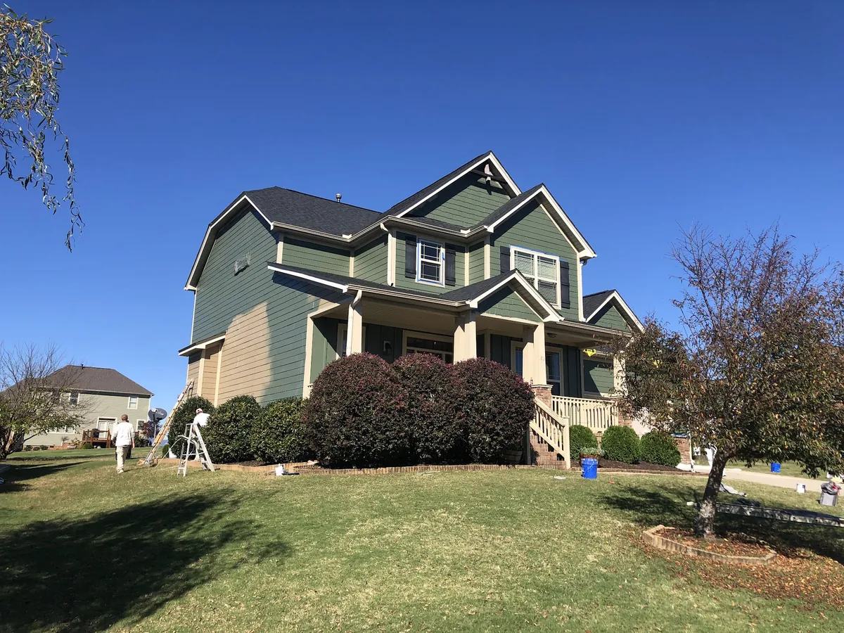Large green craftsman-style home with stone accents and a crew on ladders