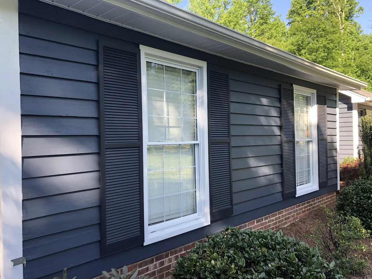 Close-up of navy siding with fresh white window trim and shutters